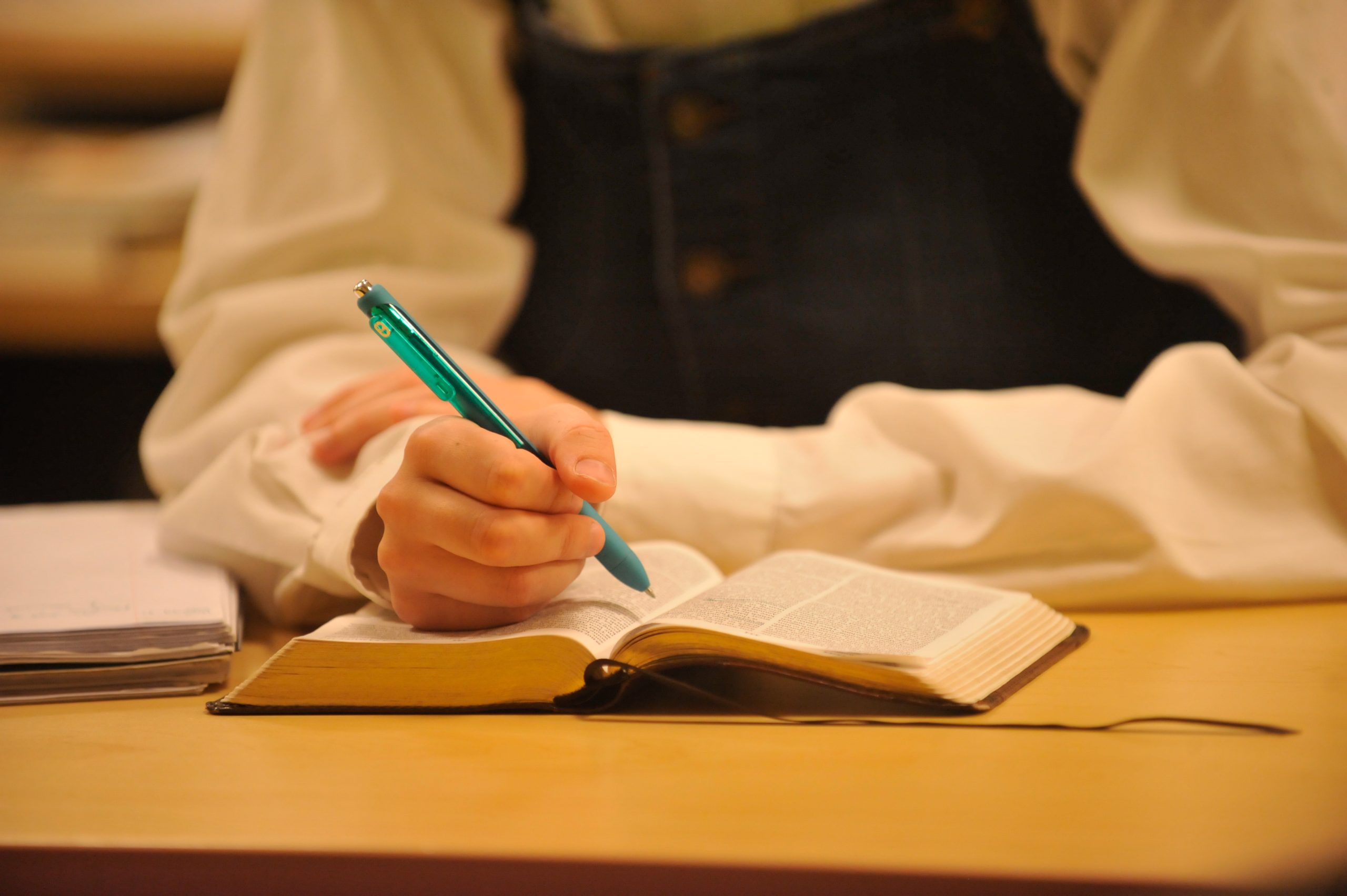 open Bible on table with female student's hands and a pen