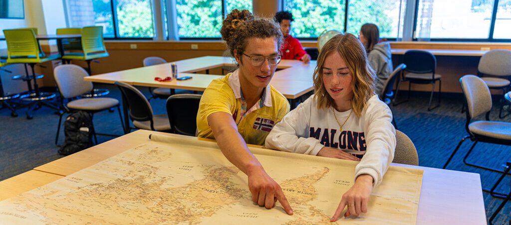 2 students sitting at a table looking at a map of the world