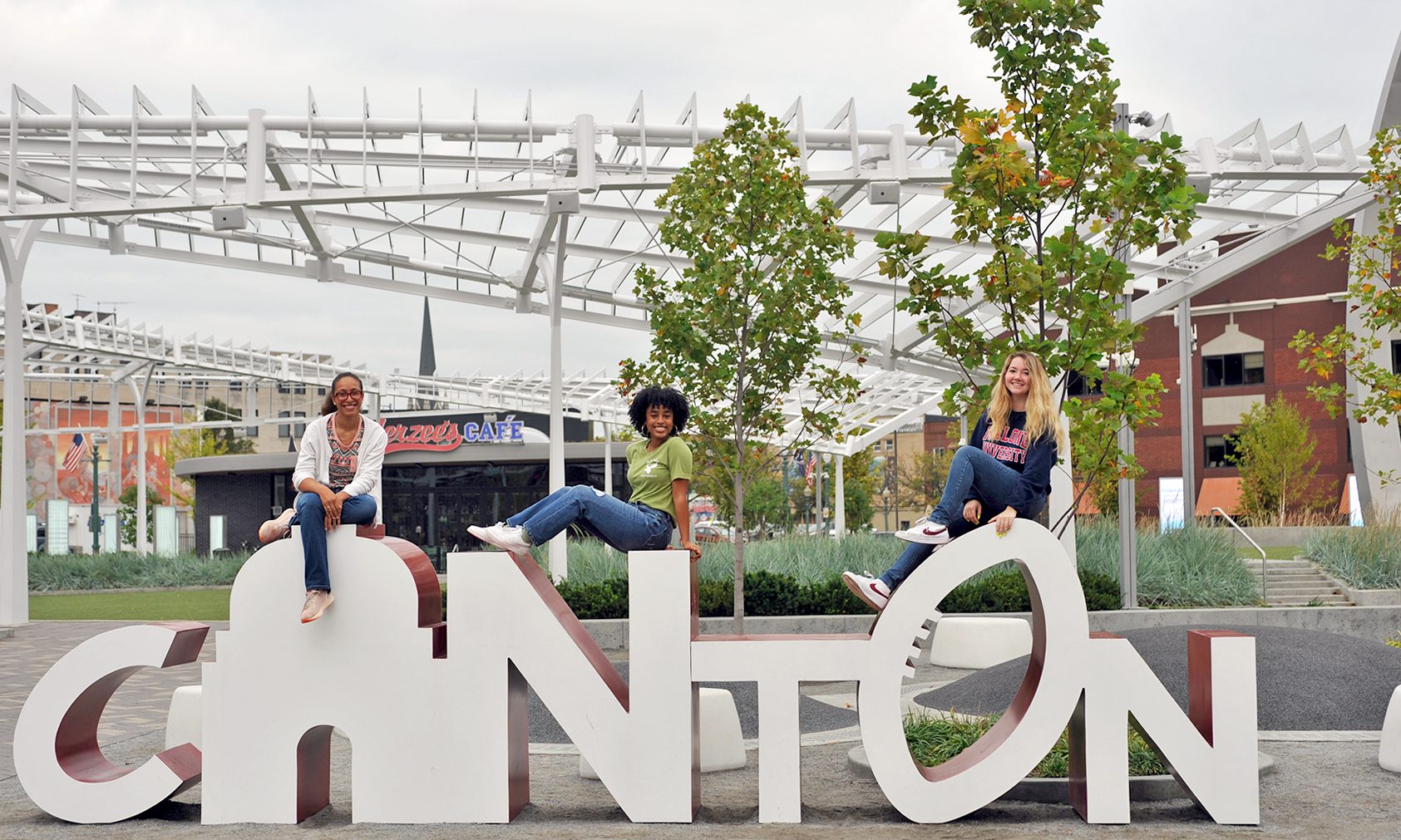 3 females seated atop outdoor large lettered platform spelling CANTON