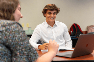 Students smiling around a table observing work on a laptop