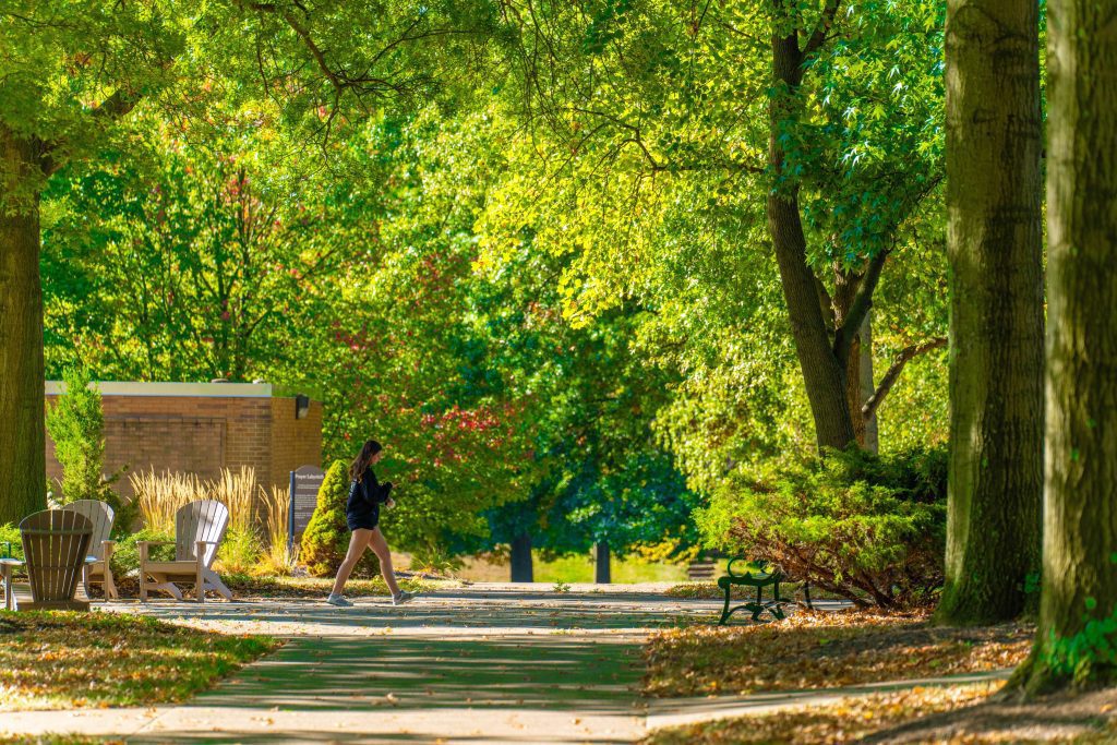 side view of girl in shorts walking on sidewalk among green trees