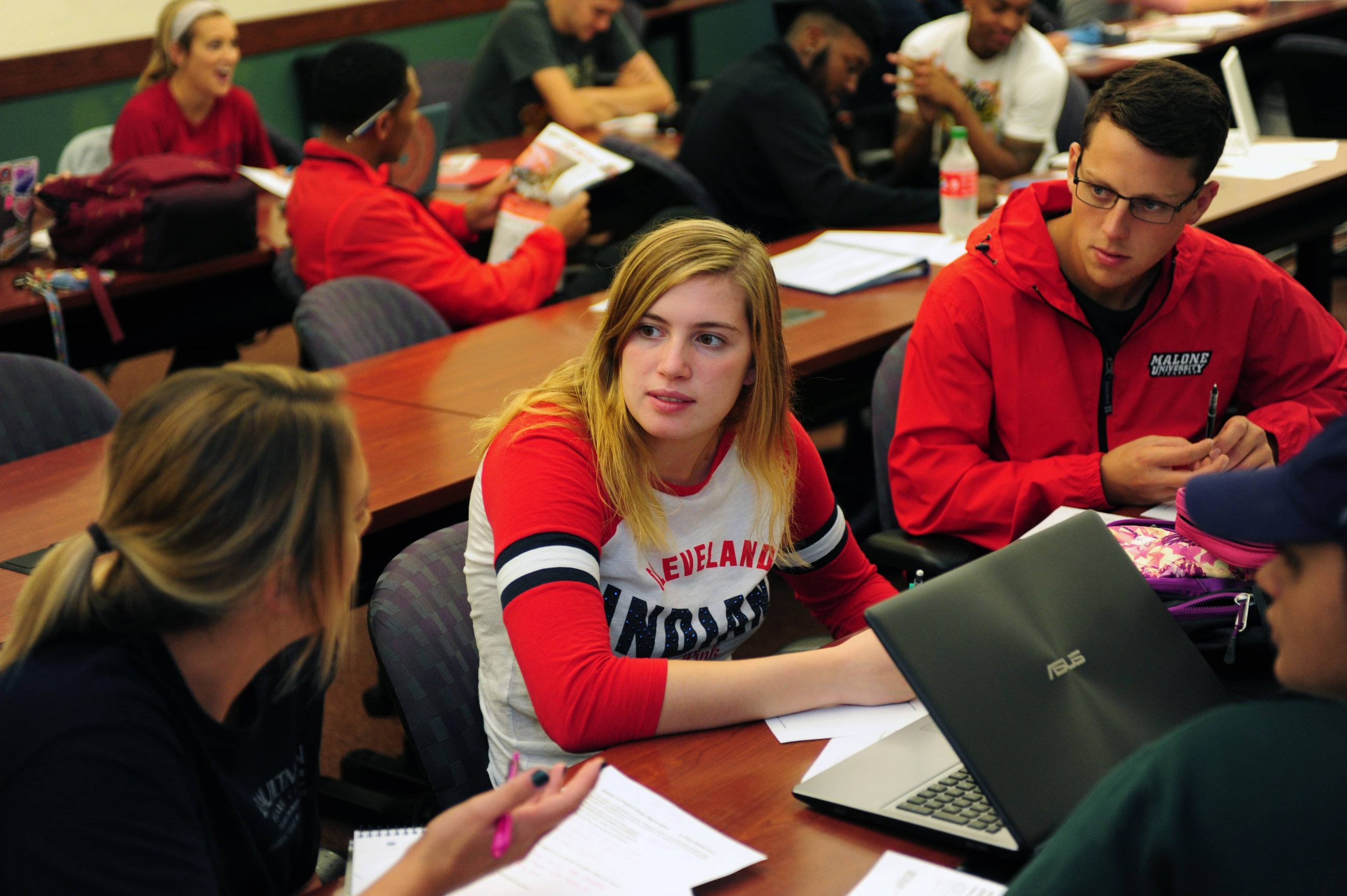business classroom; 4 students in foreground with laptop