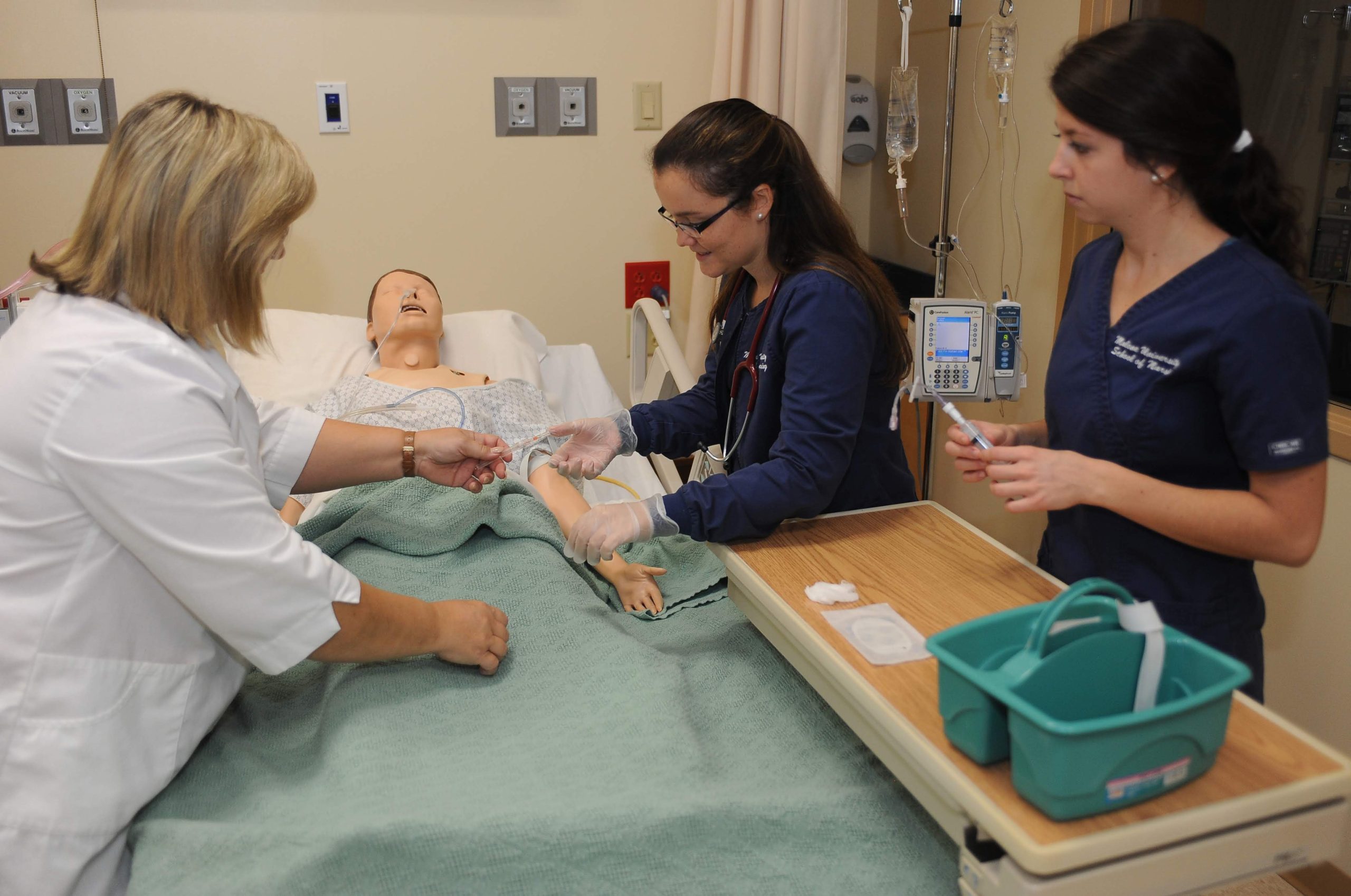 2 female nursing students and instructor practicing on "dummy"