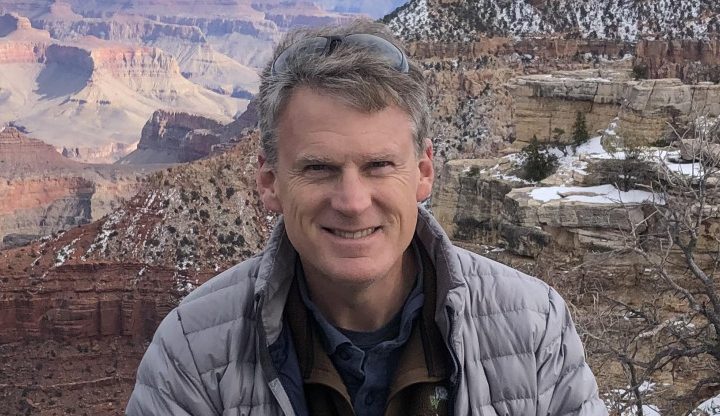 Chuck Hoover in parka with rough, beautiful terrain in background