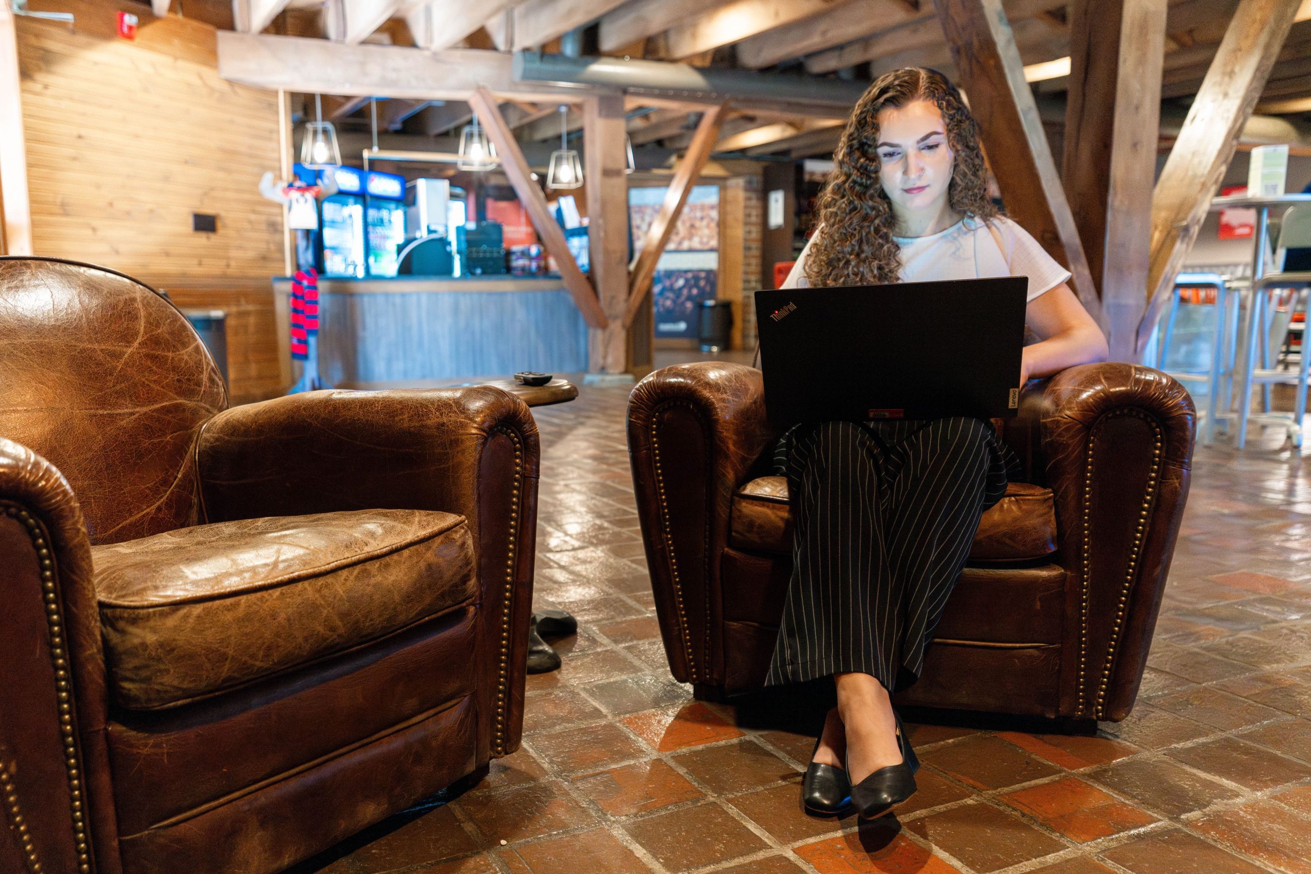 student sitting in a chair while on her laptop in a lounge