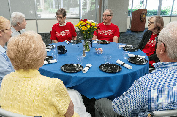Group of retired Malone supporters sit around a circle table with a blue tablecloth