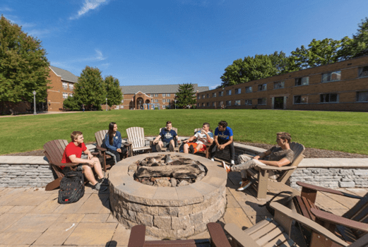 Group of six students sits outside near a fire pit with blue sky above