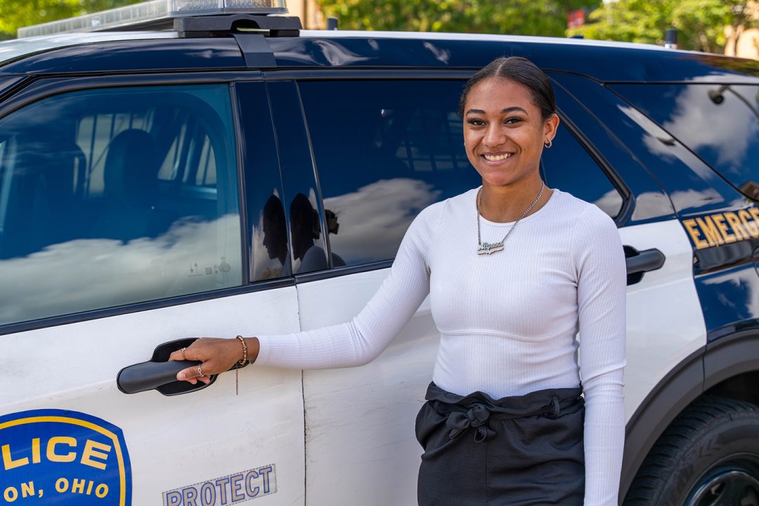 smiling female student posing in front of police vehicle