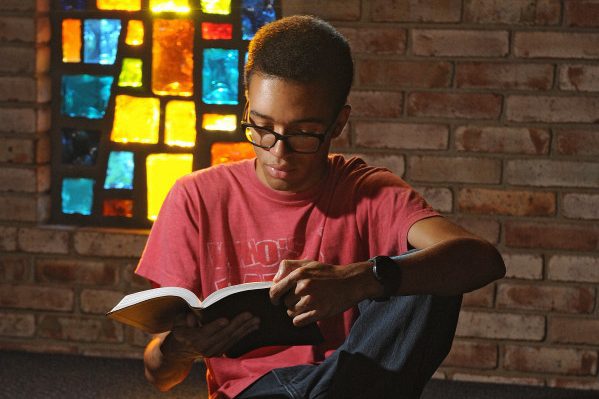 A student reading his Bible in front of a stained glass window