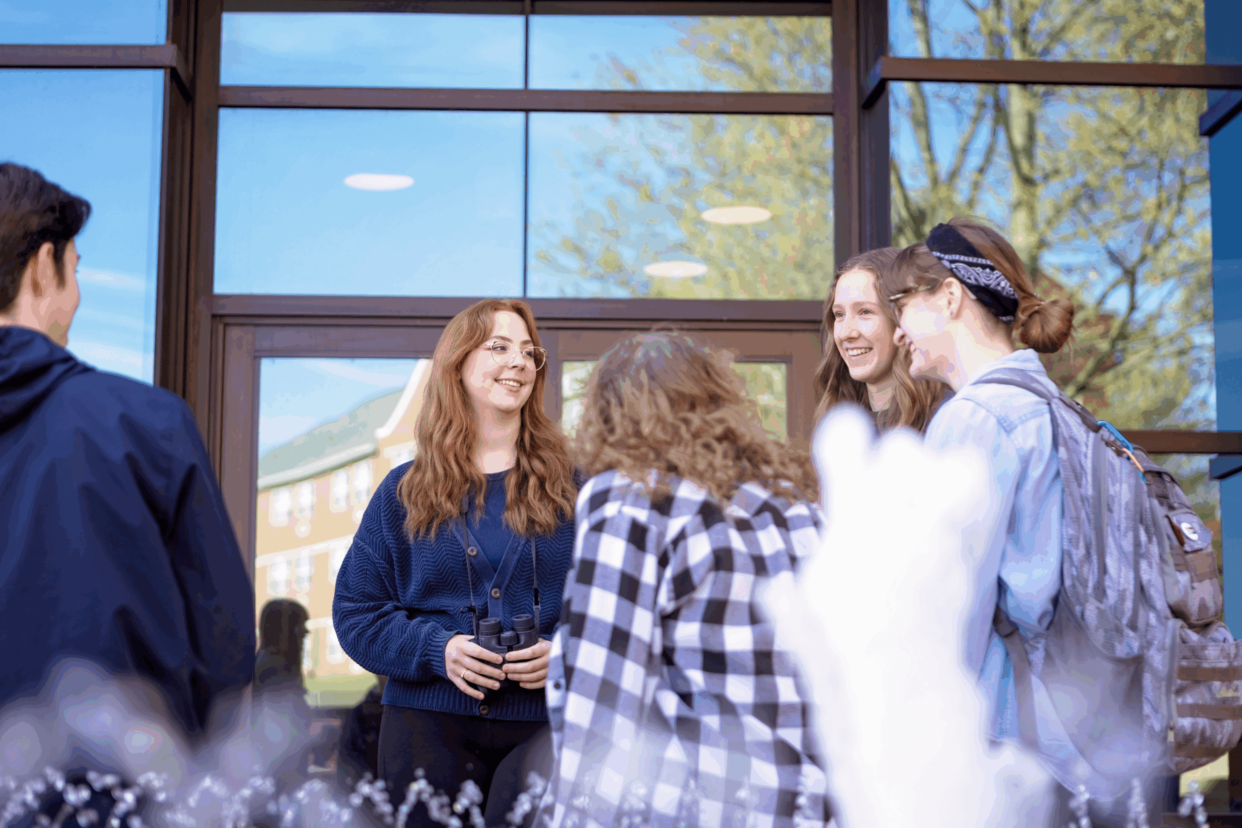 Small group of male and female Malone students stand together talking outside a glass doorway