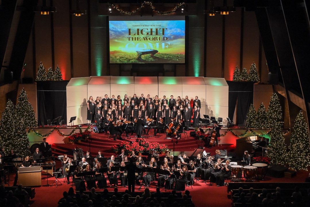 Wide angle shot of a large choir concert in the auditorium with the stage lit in red and green