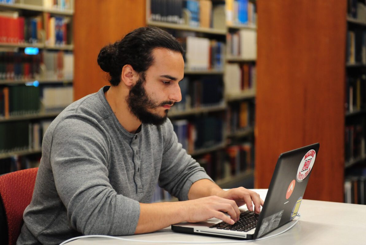 student sitting at a table while on his lap top in the library