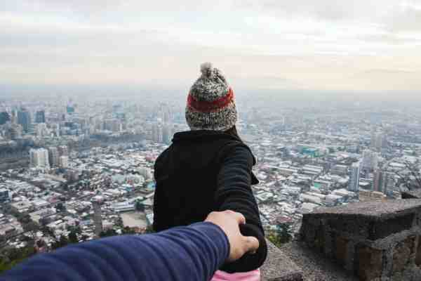 woman with her back to the camera overlooking a city while holding another person's hand