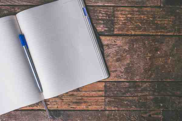 image of a blank notebook with a pen inside laying open on a wooden table
