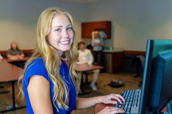 Female student standing at a computer station in the Entrepreneurship program.