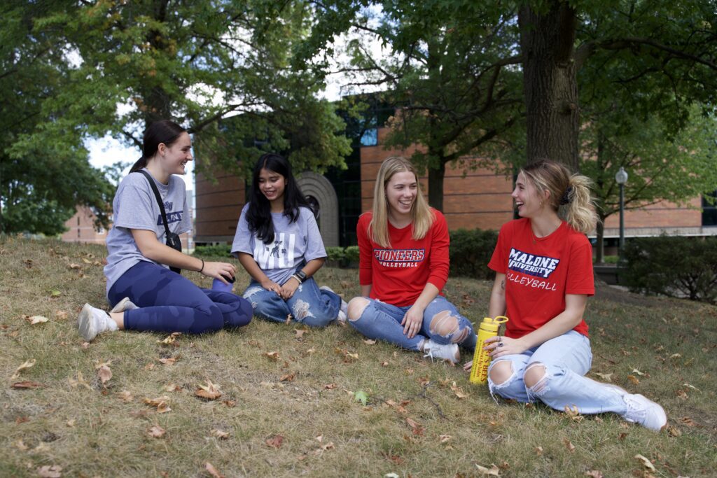 Four Malone Students sitting outside the library.